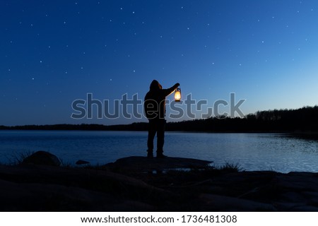 Man holding the old lamp outdoors near the lake. Hand holds a large lamp in the dark. Ancient lantern illuminates the way on a night. Light and hope concept.