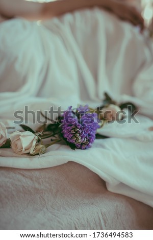 A close-up composition of white roses and purple hyacinth on a linen sheet. Floral and wellness concept.Tender morning decor. Flowers on a white tablecloth and silhouette of female body. Soft focus
