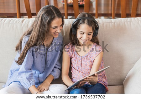 Two sisters watching media on a tablet sitting on the sofa at home