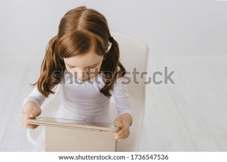 Picture of happy child with fair red curly hair with a tablet isolated on white background