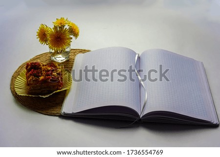 Spring breakfast, lunch - a piece of cake, a cupcake, a cake on a jute stand. A cup of flowers with yellow dandelions. On white background. View from above. And an open notebook