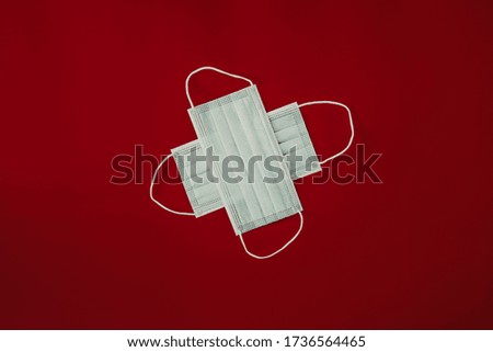 Two respiratory medical masks in the form of a medical cross on red background. Mask symbol of protection against coronavirus. Surgical mask, protection concept. COVID-19 concept