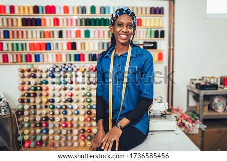 Portrait of happy african dressmaker woman in studio. Background of colorful sewing thread. Royalty-Free Stock Photo #1736585456