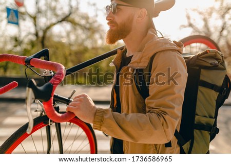 handsome hipster stylish bearded man in jacket and sunglasses walking alone in street with backpack on bicycle healthy active lifestyle traveler backpacker