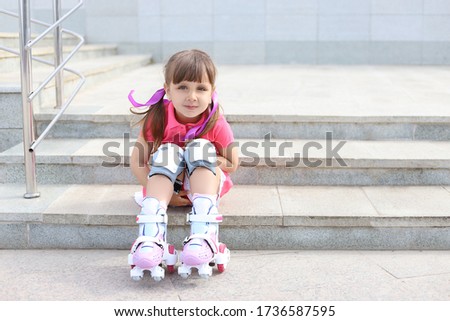 Little girl learns to roller skate. Portrait of a sporty child girl in park.