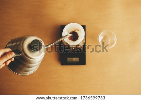 Hands pouring hot water from steel kettle in filter with ground coffee in pour over on scale , top view. Alternative coffee brewing. Barista making filter coffee Royalty-Free Stock Photo #1736599733
