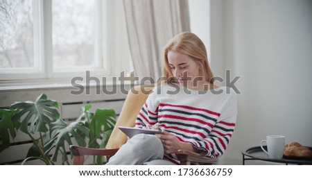 Happy young woman relaxing at home sit on sofa holding digital tablet enjoying surfing internet study work shopping online using social media apps or playing game on modern tech device at home