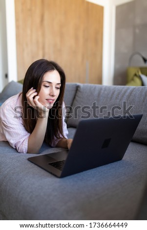 beautiful cheerful woman with happy smile lying on the sofa with laptop