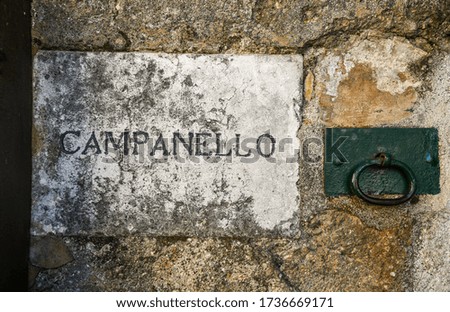 Close-up of the exterior wall of an old building with a stone plaque that says: "Doorbell" and an iron handle, Italy