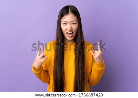 Young Chinese girl over isolated purple background making horn gesture