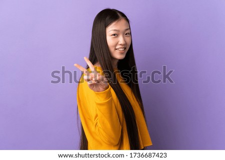 Young Chinese girl over isolated purple background smiling and showing victory sign