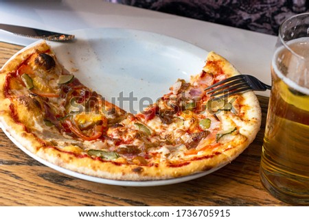 Eating a slice of fresh baked pizza with cheese and meat topping and a beer in the restaurant close up