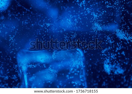 Blue sparkling water with ice cubes and bubbles macro close up