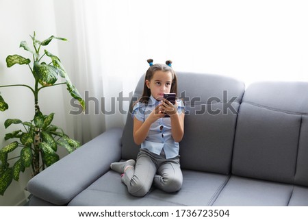 Distance learning, online education for kids. Little girl studying at home in front of the smartphone. Child watching online cartoons, kids computer addiction, parental control. Quarantine at home