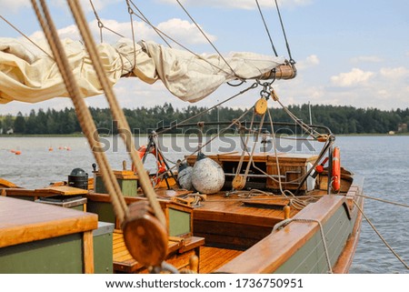 Close-up of the deck of a green and brown wooden sailboat. The boat is floating on the water on the river with white sails