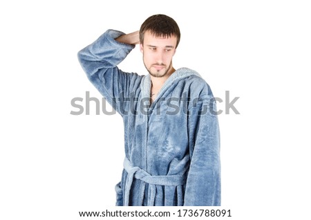 Portrait of young caucasian bearded man in blue bathrobe shows clueless emotion isolated on white background