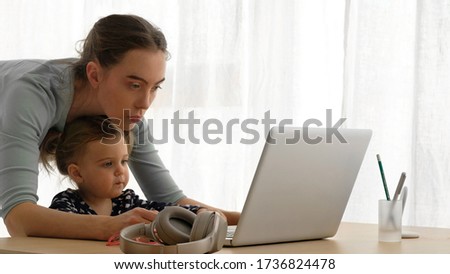 Young woman and toddler watching cartoon together on netbook in bright living room while relaxing during weekend