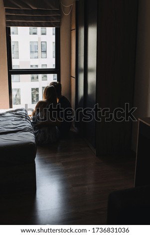 A guy with a girl sitting in front of the window waiting for the end of quarantine