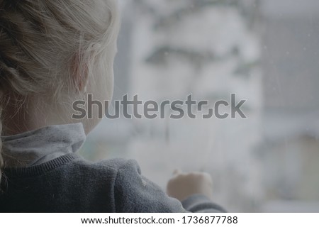 Preschool girl draws on the window, which reveals a heart. Cute little girl drawing heart shape with two fingers on fogged window.