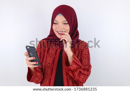 Young Asian Islam woman wearing headscarf is smile and shy with what she see on the smartphone.