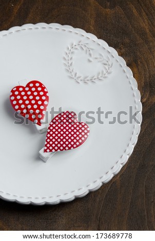 Valentines Day table setting place. Red Hearts on a white plate on wooden background.
