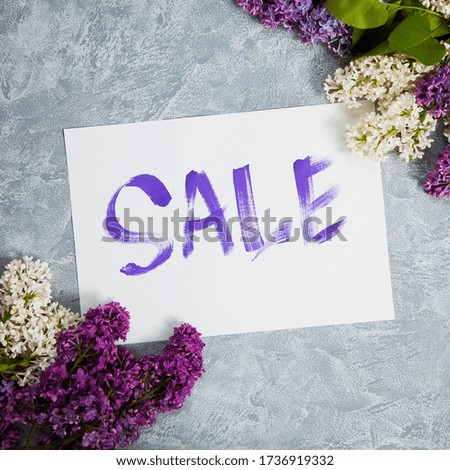 Handwritten word sale in white frame lay in lilac blossom. Square picture of discount promotion. Shopping concept.