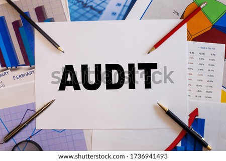 The word AUDIT written on a white sheet of paper on the background of graphs next to pencils