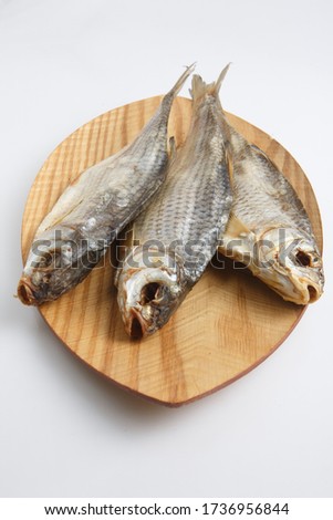 close up top view shot of three Russian dried salted vobla (Caspian Roach) fish on a wooden plate on a white background
