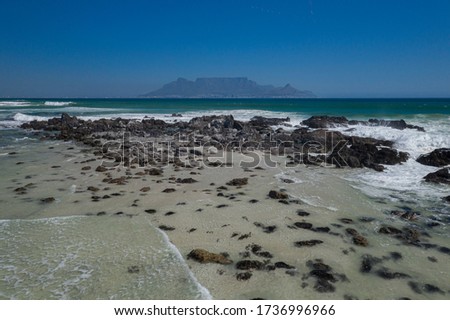 A sandy beach with rocky shoreline with Table Mountain and the blue sea in the background 