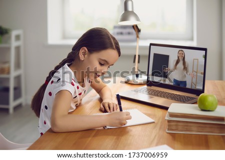 Online training. The teacher teaches the child a video call chat classroom video conferencing. Little girl teach a lesson using a laptop with sitting at a table at home.