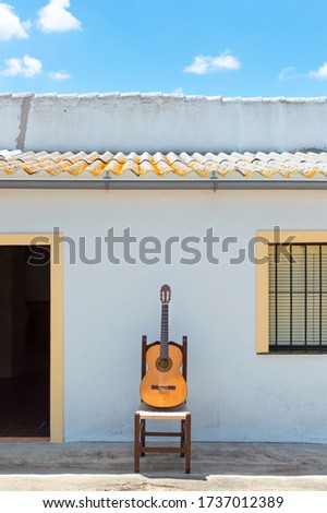 Spanish guitar in front of the white facade of a beautiful house in the countryside on sunny day with clear sky. Flamenco or andalusian concept.