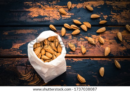 Paper bag stuffed with roasted almonds on a dark brown wooden background, close up, top view, copy space
