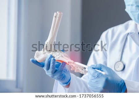An orthopedic doctor looking at a fake ankle bone Male doctors orthopedic wears medical masks and medical gloves To analyze the causes of ankle degeneration in the office at the hospital Royalty-Free Stock Photo #1737056555