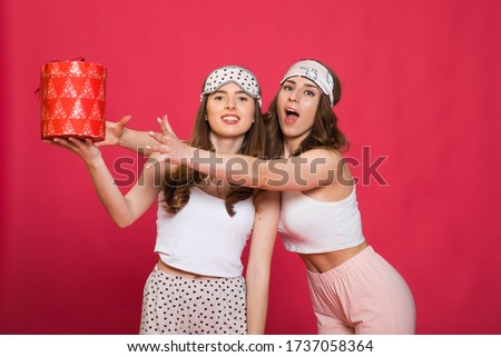 beautiful and attractive woman gives a box with gift to her teenager daughter on a pink background in the studio . the concept of celebrating the mother's day and birthday