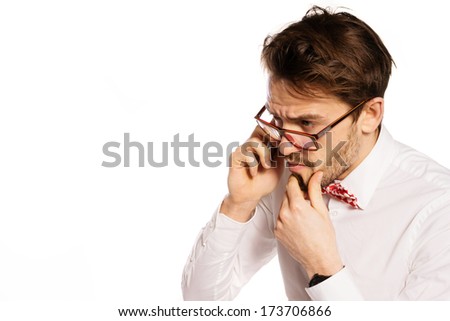 Nerdy bearded businessman wearing glasses and a polka dot bow tie frowning as he listens to the conversation while talking on a smartphone, isolated on white