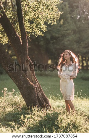 Portrait of a beautiful young blond woman white round beads, pearls, jewelry in a white dress in a boho style walks in the park in summer at sunset.