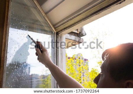 Rubber squeegee in male hand cleans a soaped window. Picture with selective focus. House cleaning, washing windows.