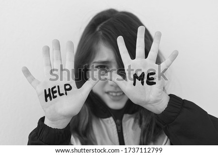 Young school girl (female age 10) being bullied in school protecting her face with her hands with the words writing over her hands Help Me concept looking at camera.