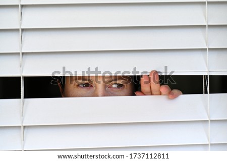 Suspicious person looking outside home window from behind Venetian curtains. Concept photo of person that have Pistanthrophobia and Agoraphobia, a person who don't trust fear of leaving the house.  Royalty-Free Stock Photo #1737112811