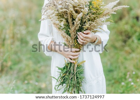 Portrait of a young girl in white dress holding big bouquet of wild flowers in the summer park.