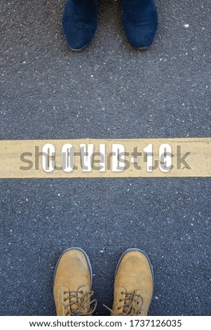 Closeup of feet standing on the road with yellow line between the two - Social Distancing  concept 