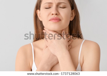 Young woman checking thyroid gland on grey background