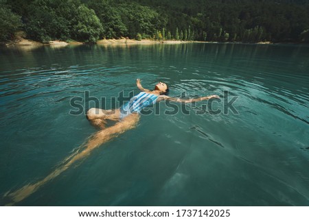 traveler carefree woman relaxing and floating in calm clear water, swimming on back in blue lake. Outdoor adventure, people in nature and calmness concept