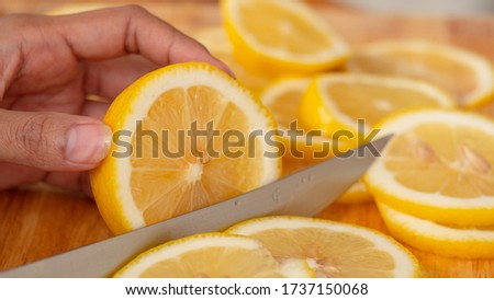 Hand holding a knife cutting Lemon,  The chopping block is full of sliced ​​lemon.
