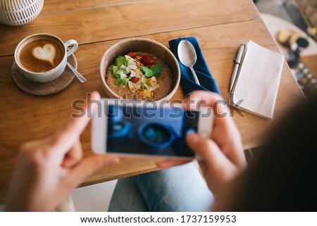 Cropped image of female millennial influencer using smartphone camera for taking picture of her lunch dishes, from above picture of woman blogger making photo of food flatly on table holding cellular