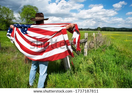 Man wearing cowboy hat standing in grass agricultural field, American flag over his shoulders, democracy, freedom, business, conservative, America, Memorial Day, Veterans Day, conservative, voters