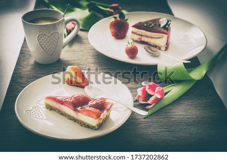 Breakfast in retro cheese, two white plates with beautiful fresh cakes and strawberries. A pink tulip flower on the edge. On the left, a mug with a heart and a good morning coffee.