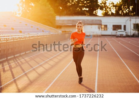 Young woman running during sunny morning on stadium track. Picture of young attractive fitness girl jogging. Athletic girl running.