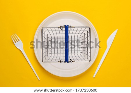 Supermarket basket in plastic plate with fork and knife on yellow background. Food purchase. Top view