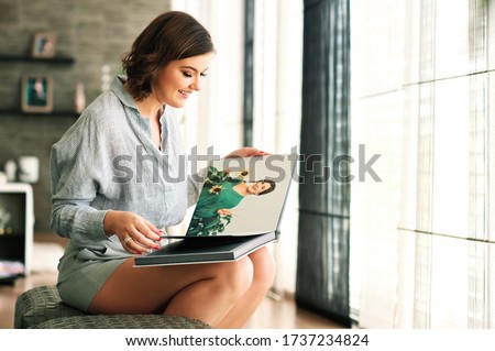 Young happy woamn looking at photo album, resting in cozy living room Royalty-Free Stock Photo #1737234824